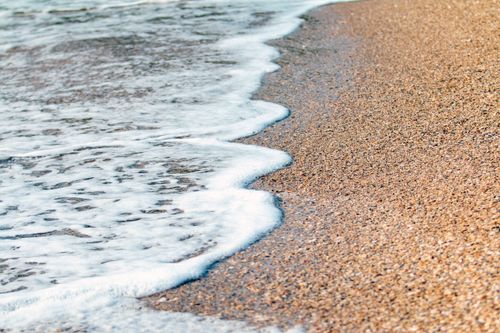 Free A detailed look at waves gently washing onto a sandy beach, capturing the tranquility of the ocean. Stock Photo