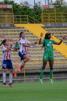 Dynamic shot of women footballers jumping for the ball during a stadium match.