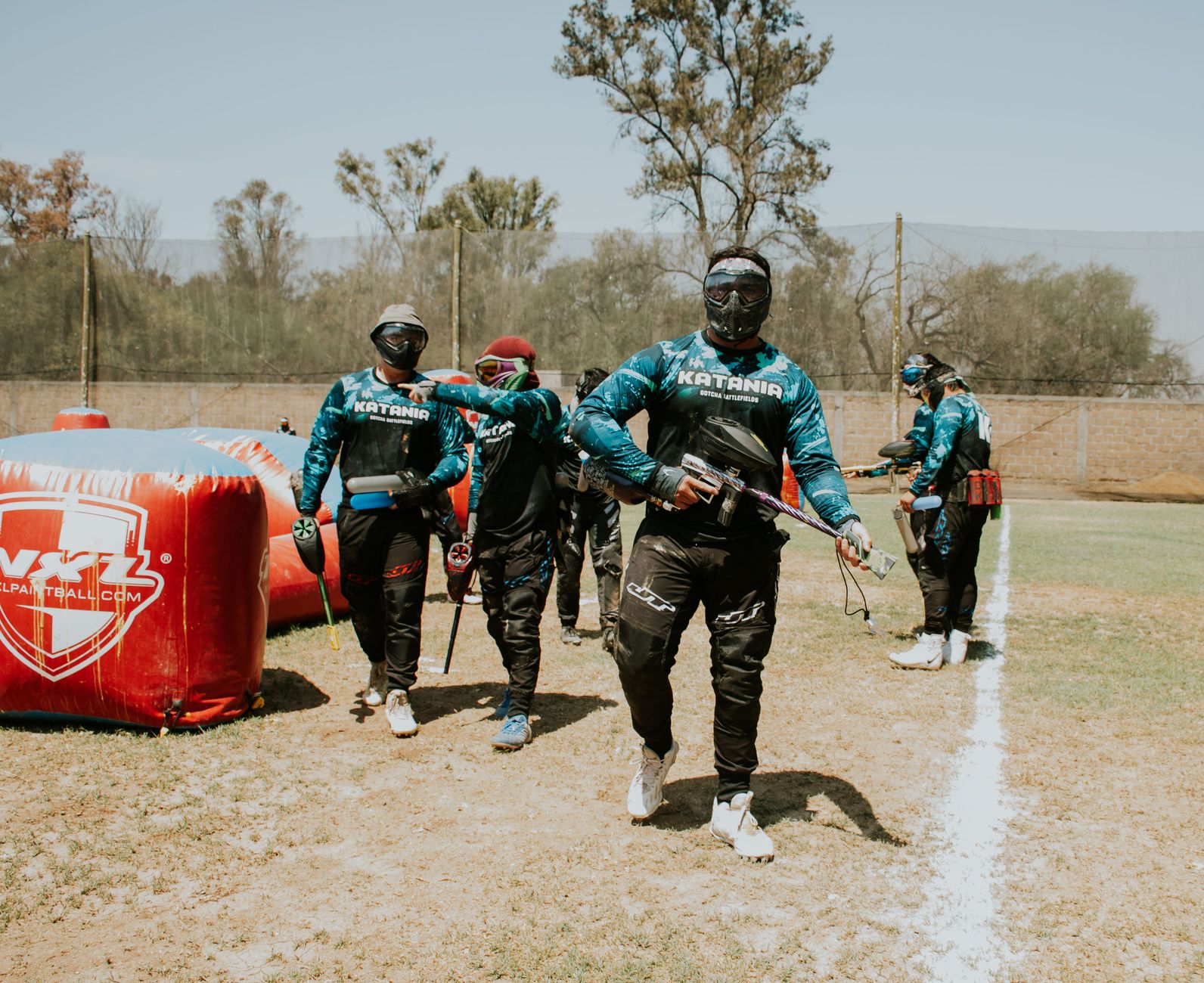 A group of paintball players in full gear walk on an outdoor field, ready for action.