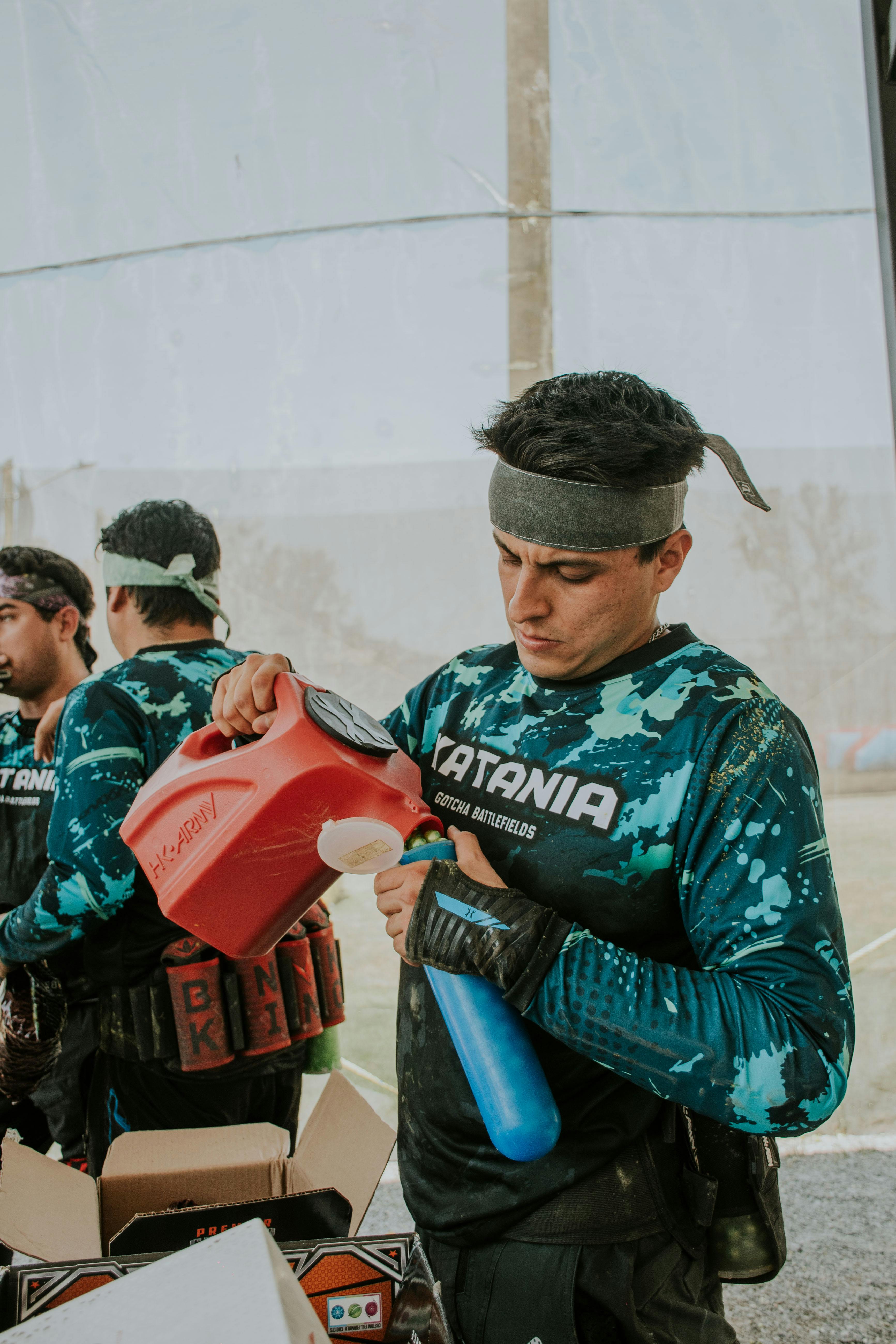 Junger Mann füllt Paintball-Markierungstank auf Außenfeld nach. Prescription Goggle Inserts - Young man refilling paintball marker tank at outdoor field.