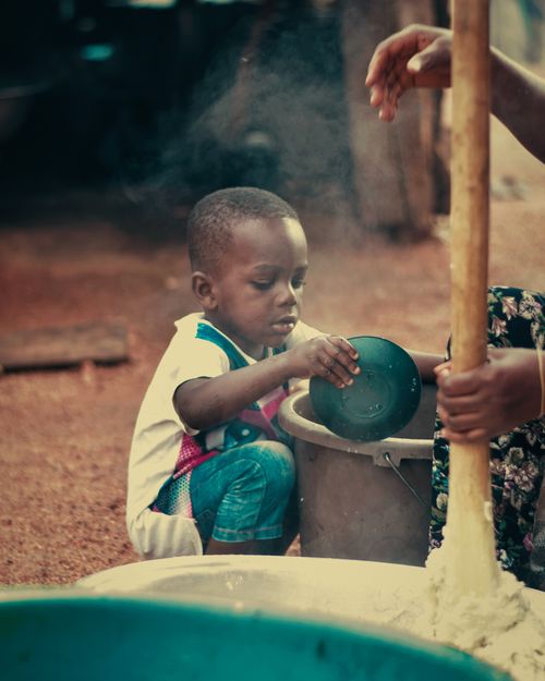 Free A child engaged in playful activities in an African outdoor kitchen, interacting with cooking utensils. Stock Photo
