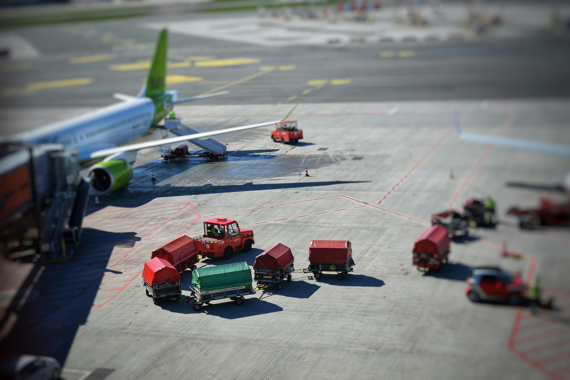 Sunlit airplane and baggage carts on airport tarmac, captured from above, showcasing transportation dynamics.