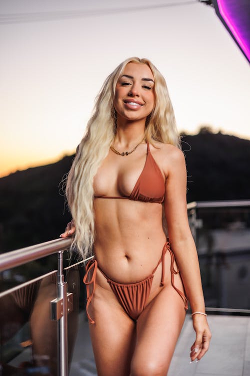 Smiling Woman in a Brown Bikini Posing on the Balcony at Sunset