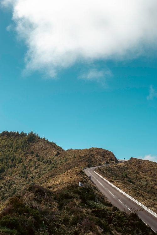 Free Scenic mountain road leading into the horizon under a bright blue sky and fluffy clouds. Stock Photo