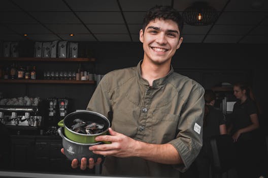 A cheerful chef proudly showcasing freshly cooked mussels in a cozy indoor setting.