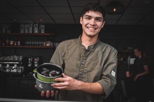 Free A cheerful chef proudly showcasing freshly cooked mussels in a cozy indoor setting. Stock Photo