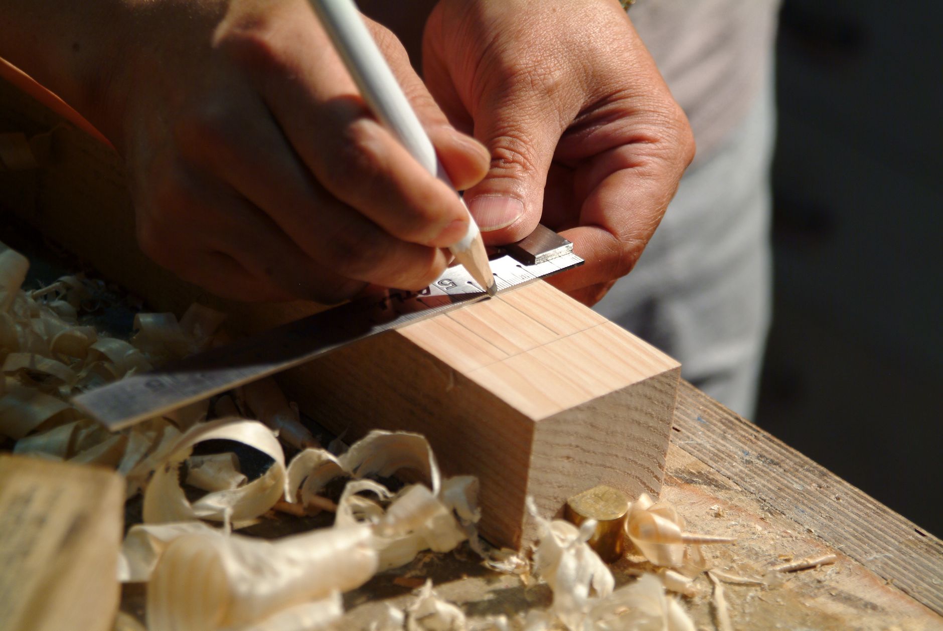 Close-up of hands measuring a wooden plank using a ruler and pencil on a workbench.