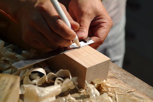 Close-up of hands measuring a wooden plank using a ruler and pencil on a workbench.