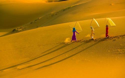 Women in Traditional Clothing Walking with Kites on Desert