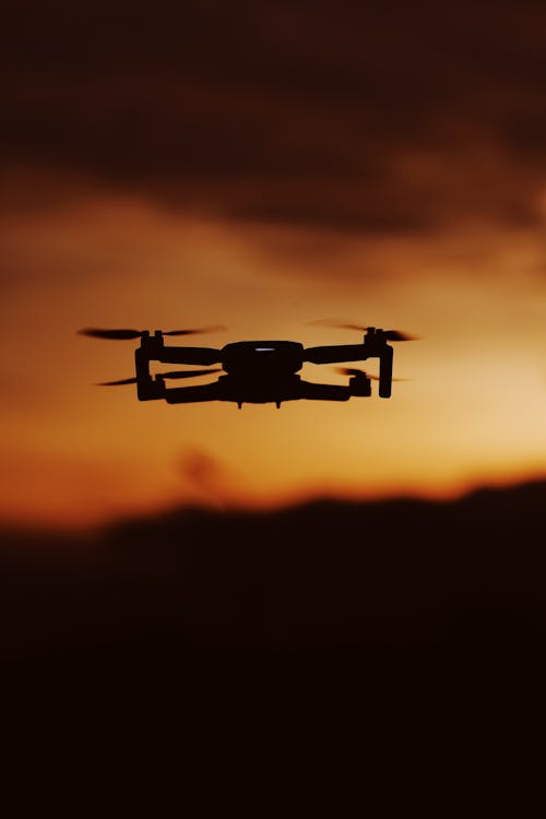 Free Silhouetted Drone Flying on the Background of a Sunset Sky  Stock Photo