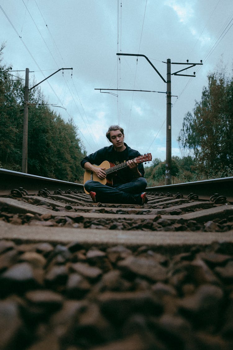 Men Playing The Guitar Sitting On The Tracks