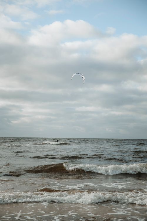 Free A kitesurfer enjoys the sea waves under a sky filled with clouds, showcasing the thrill of kitesurfing. Stock Photo