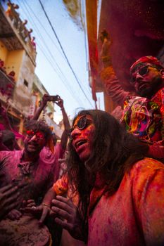 People enjoying the colorful Holi festival on a narrow street, covered in vibrant powders.