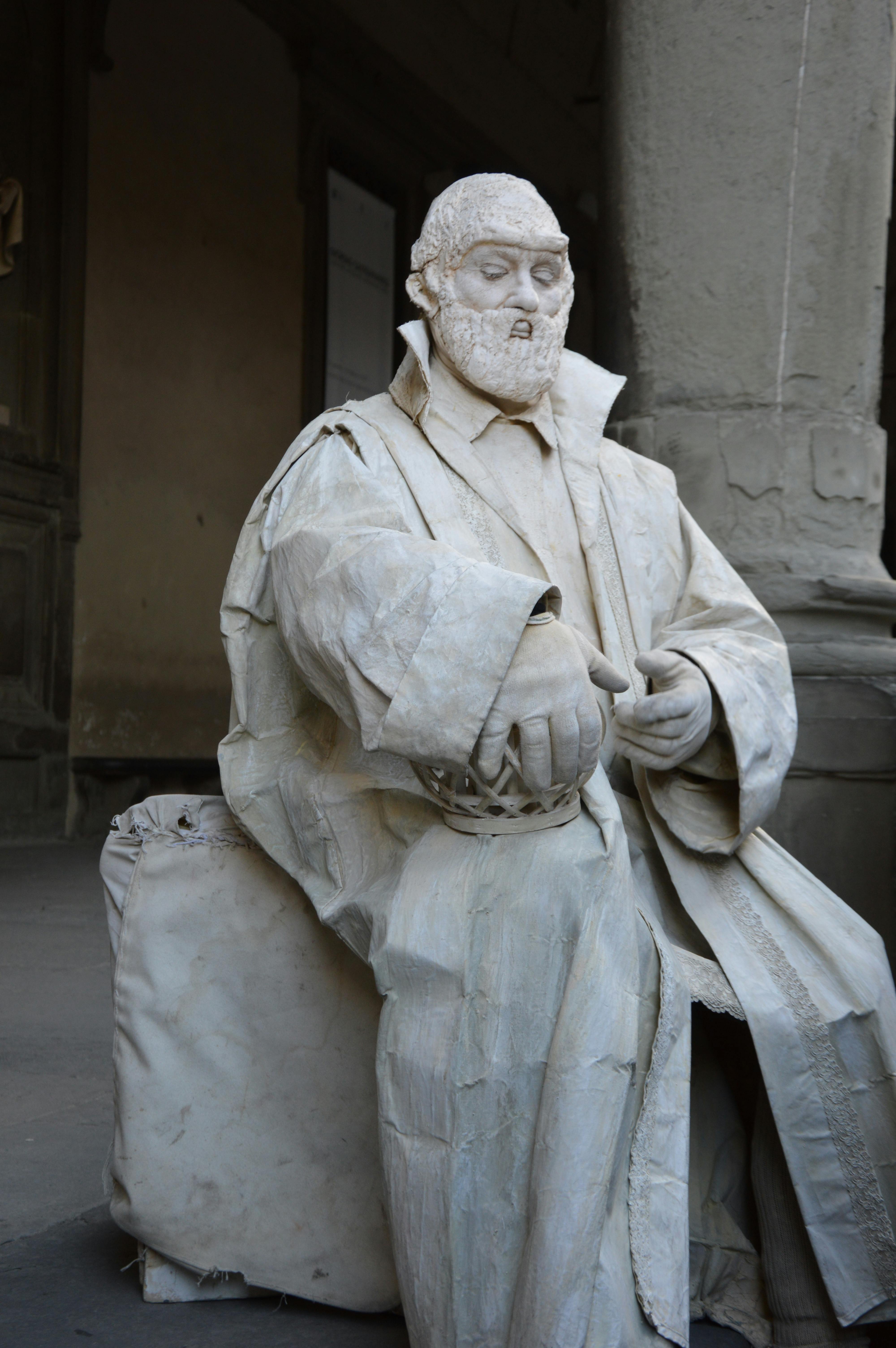 Intricately carved marble statue depicting a historical figure seated in an open gallery setting.