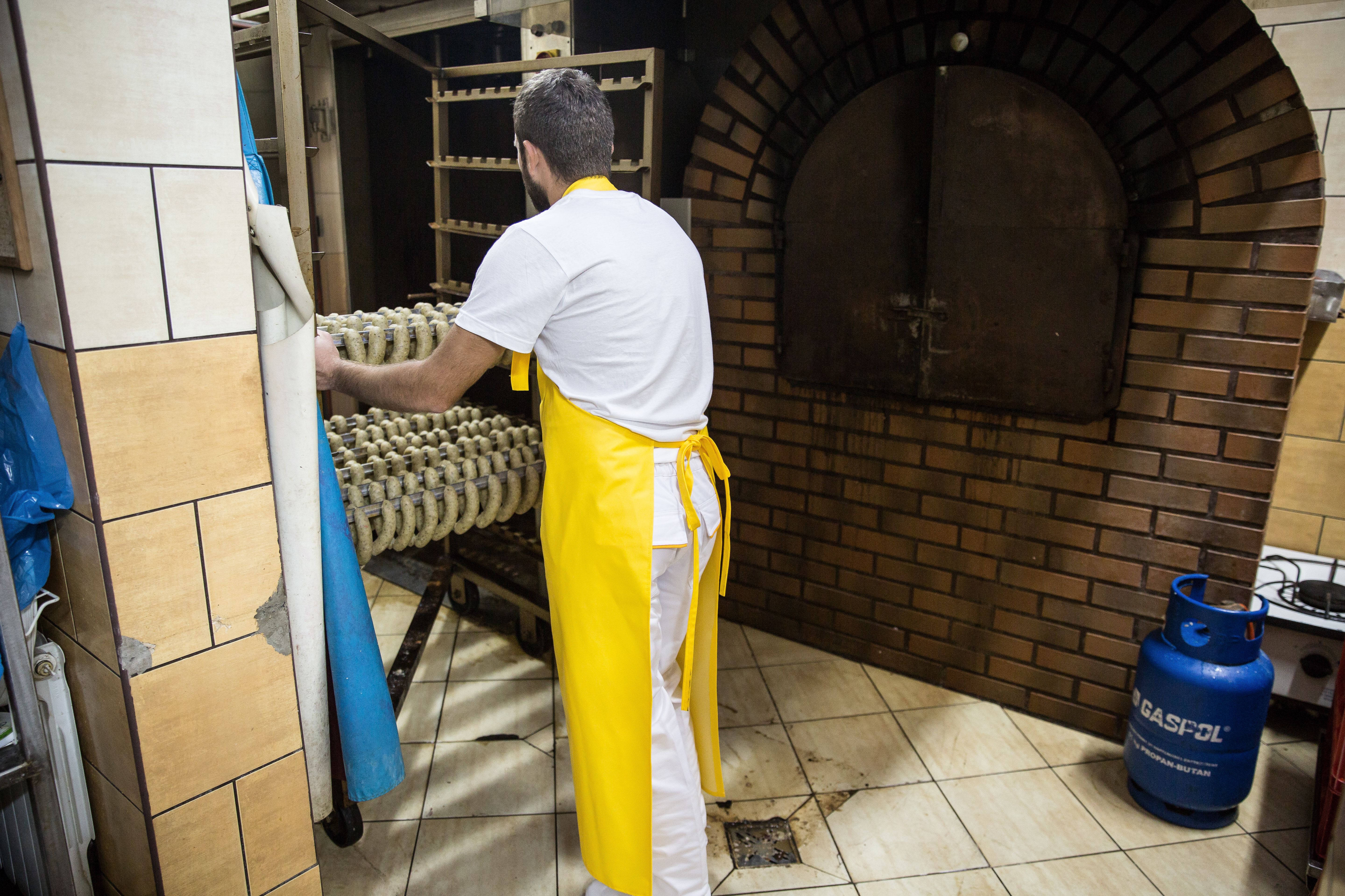 Back view of a man in a bakery wearing a yellow apron, preparing dough for baking.