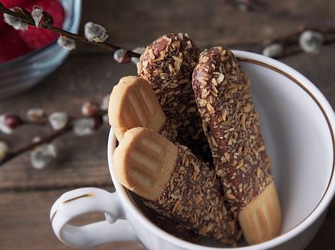 Close-up of delicious chocolate-covered biscuits garnished with nuts in a decorative cup.