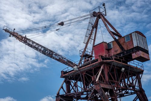 Free Rusty crane structure contrasting with a blue sky and scattered clouds. Stock Photo