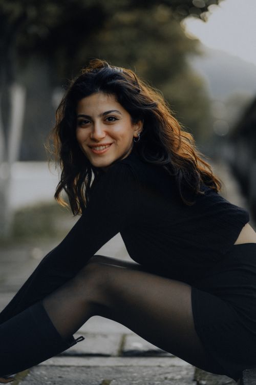 Free A woman in black clothes smiles while posing on a pavement in Fethiye, Türkiye. Stock Photo