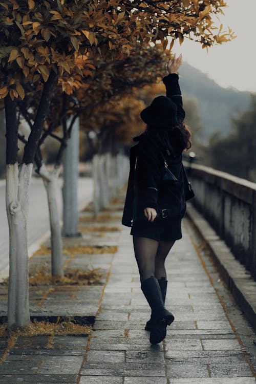Woman in Black Clothes Posing with Arm Raised under Tree on Pavement