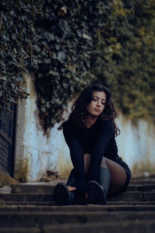Free A fashionable woman with long hair poses on stairs surrounded by ivy in Fethiye, Türkiye. Stock Photo
