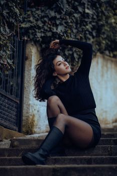 Young woman in black outfit sitting on steps, styled for a fashion shoot in Fethiye, Türkiye.