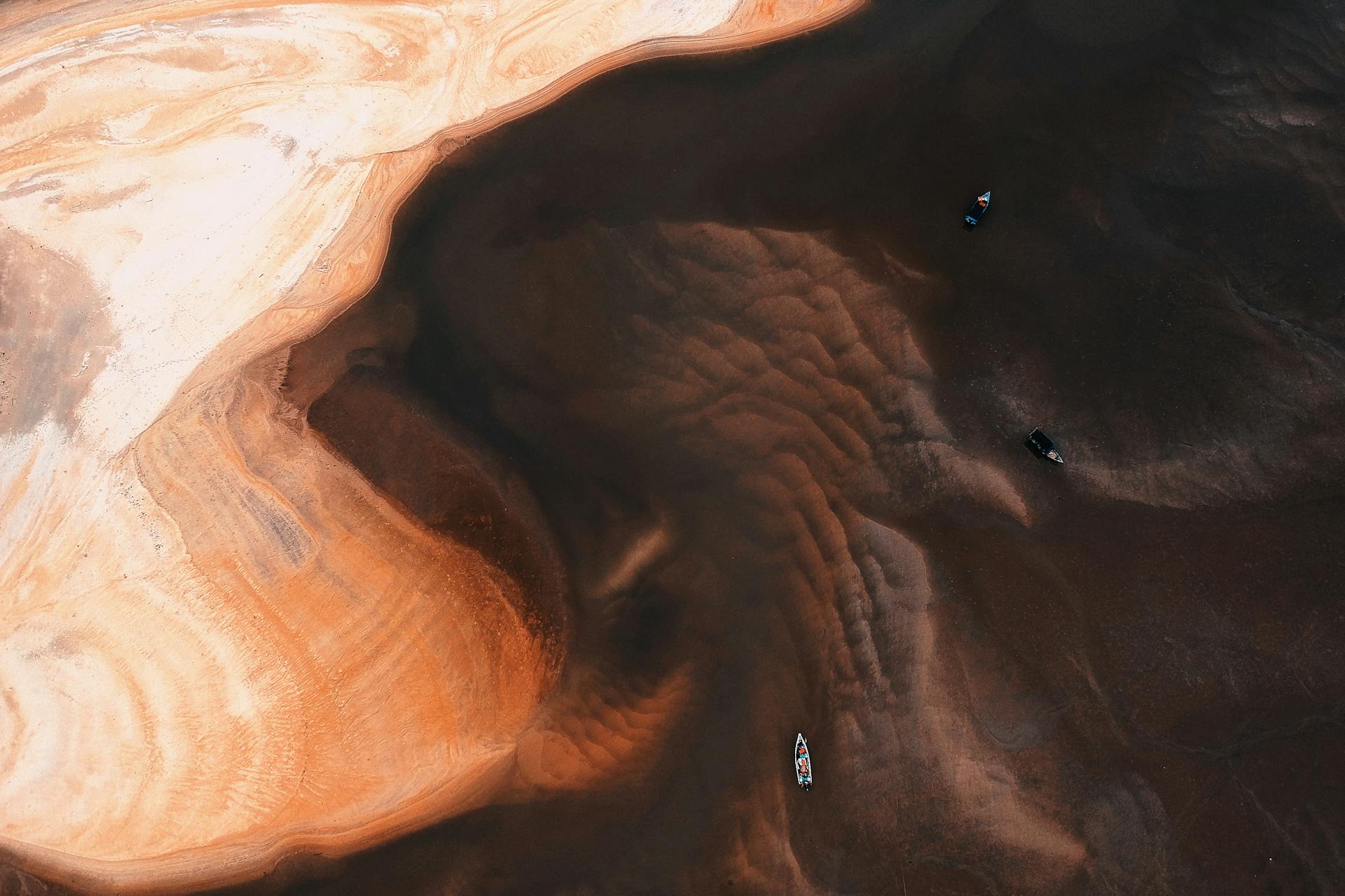Stunning aerial perspective of vibrant sand patterns and boats on a Malaysian beach.