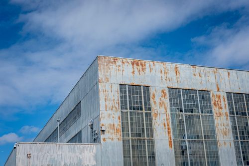 Free A low angle view of a rusty industrial building under a bright blue sky with clouds. Stock Photo
