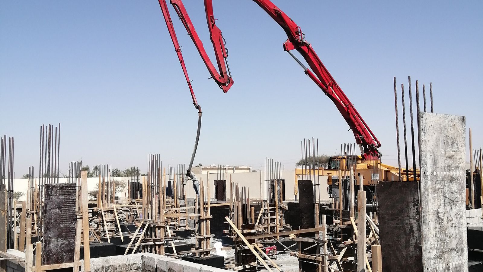 Red concrete boom pump extended over a construction site against a clear blue sky