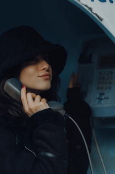 A fashionable woman in black attire using an old telephone booth in Fethiye, Türkiye.