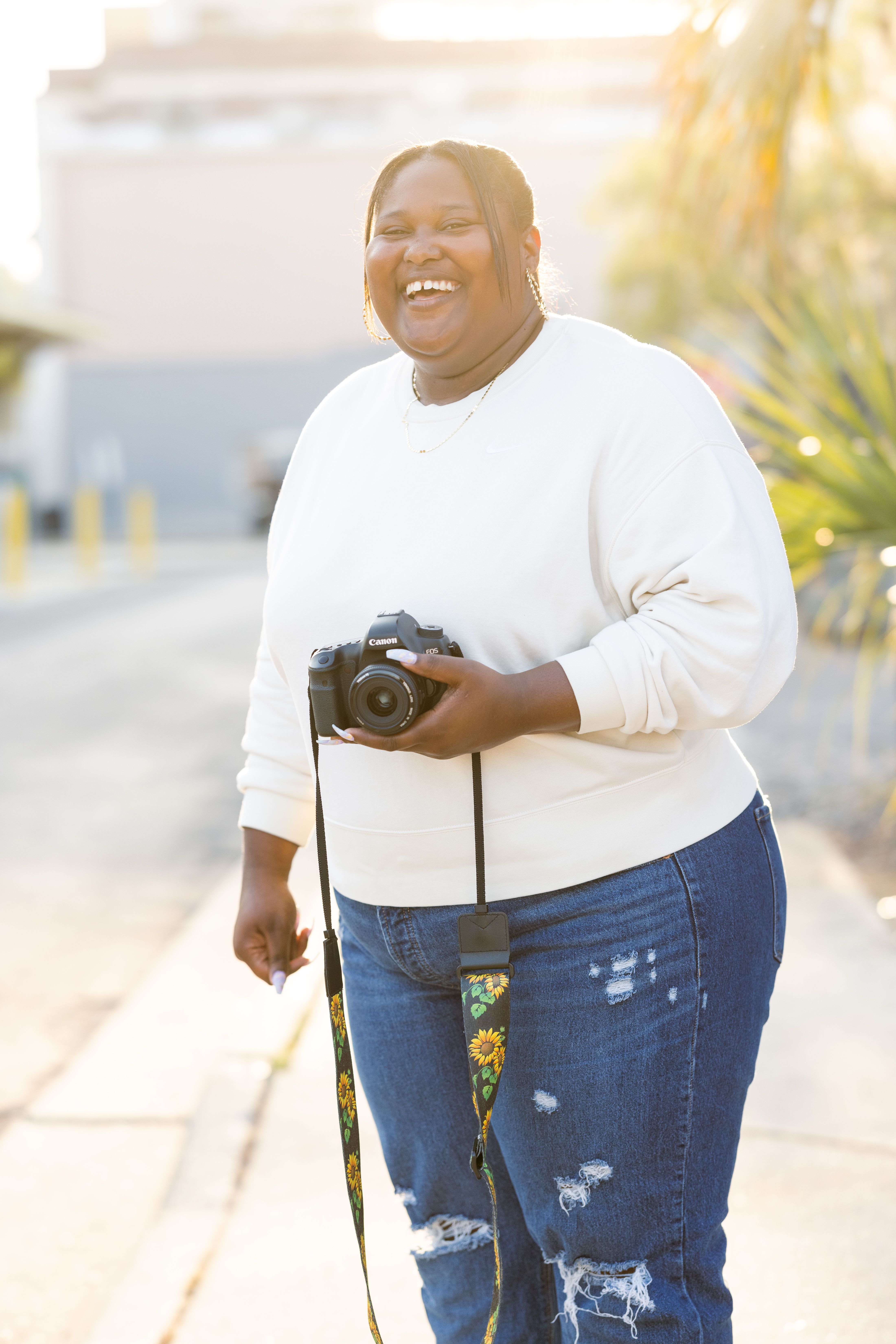 Smiling woman with a camera in an outdoor setting, exuding joy and enthusiasm.