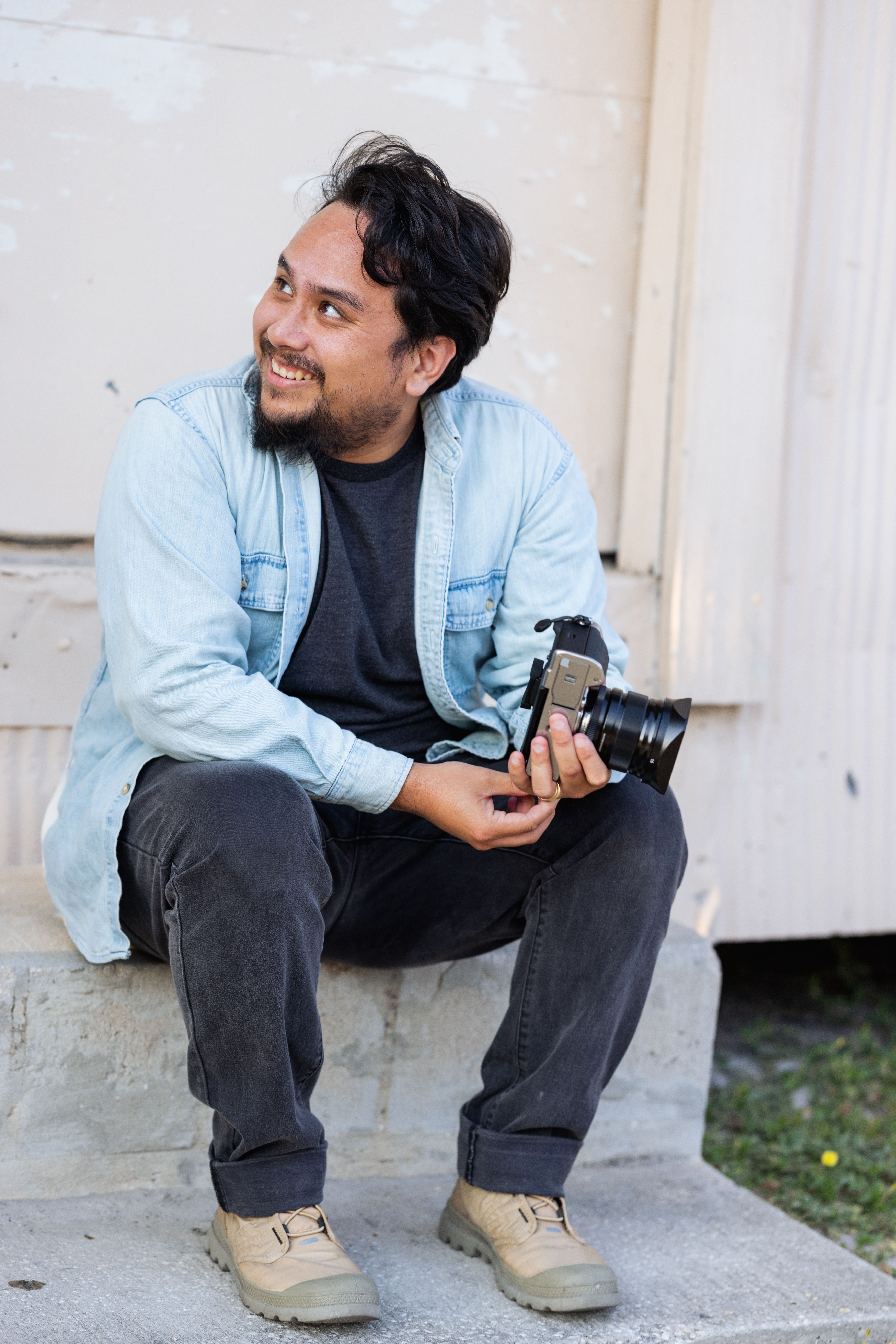 Smiling photographer sitting outdoors with a camera, looking away.