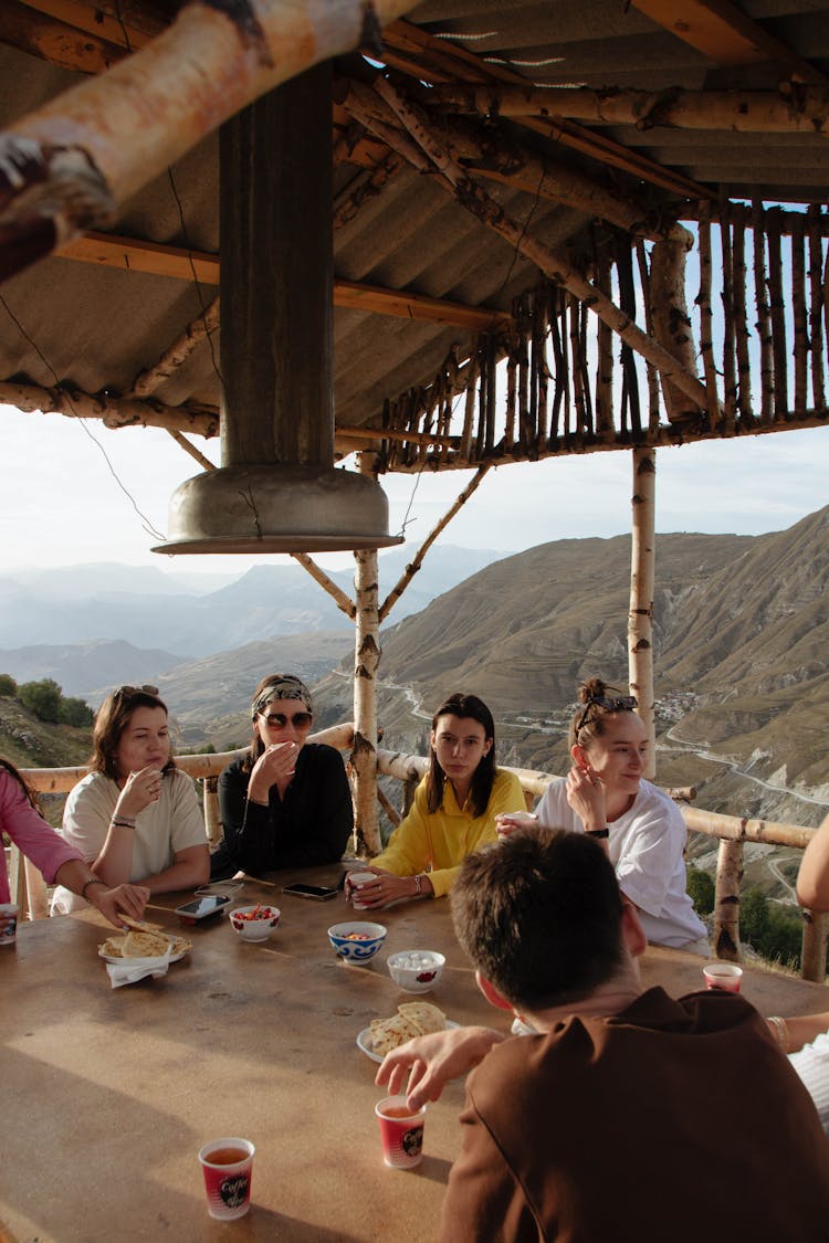 People Sitting Together At A Table With Hills Behind