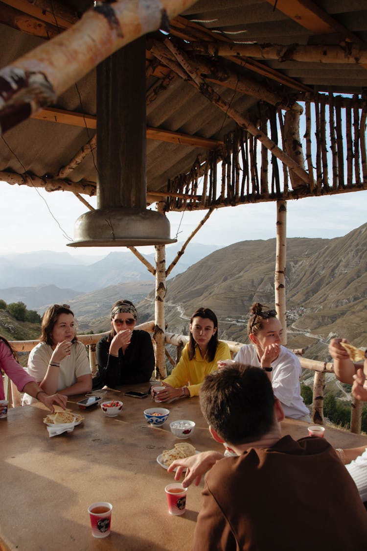 People Sitting Together At A Table With Hills Behind