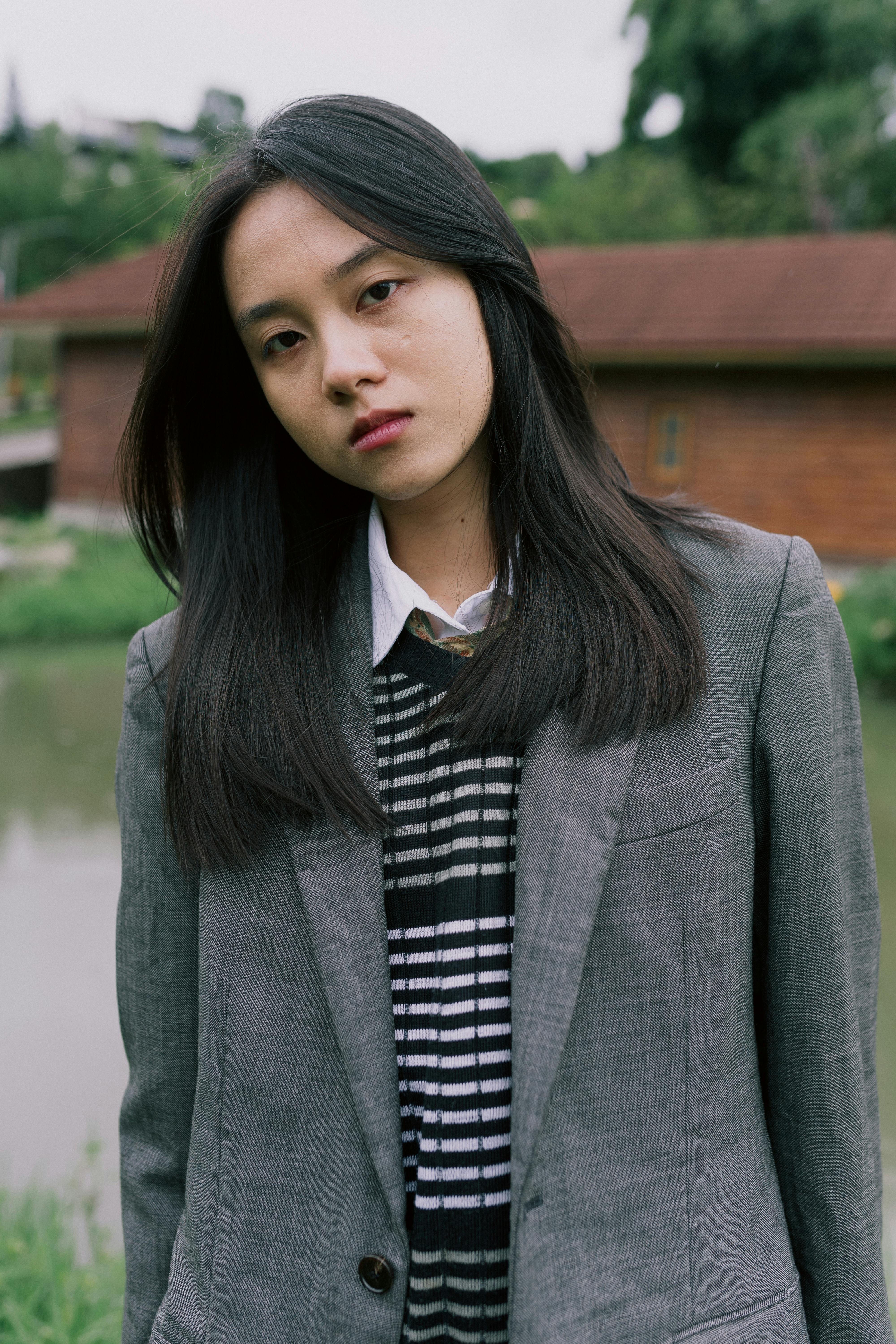 Portrait of a young woman in a gray blazer, standing outdoors with natural background.