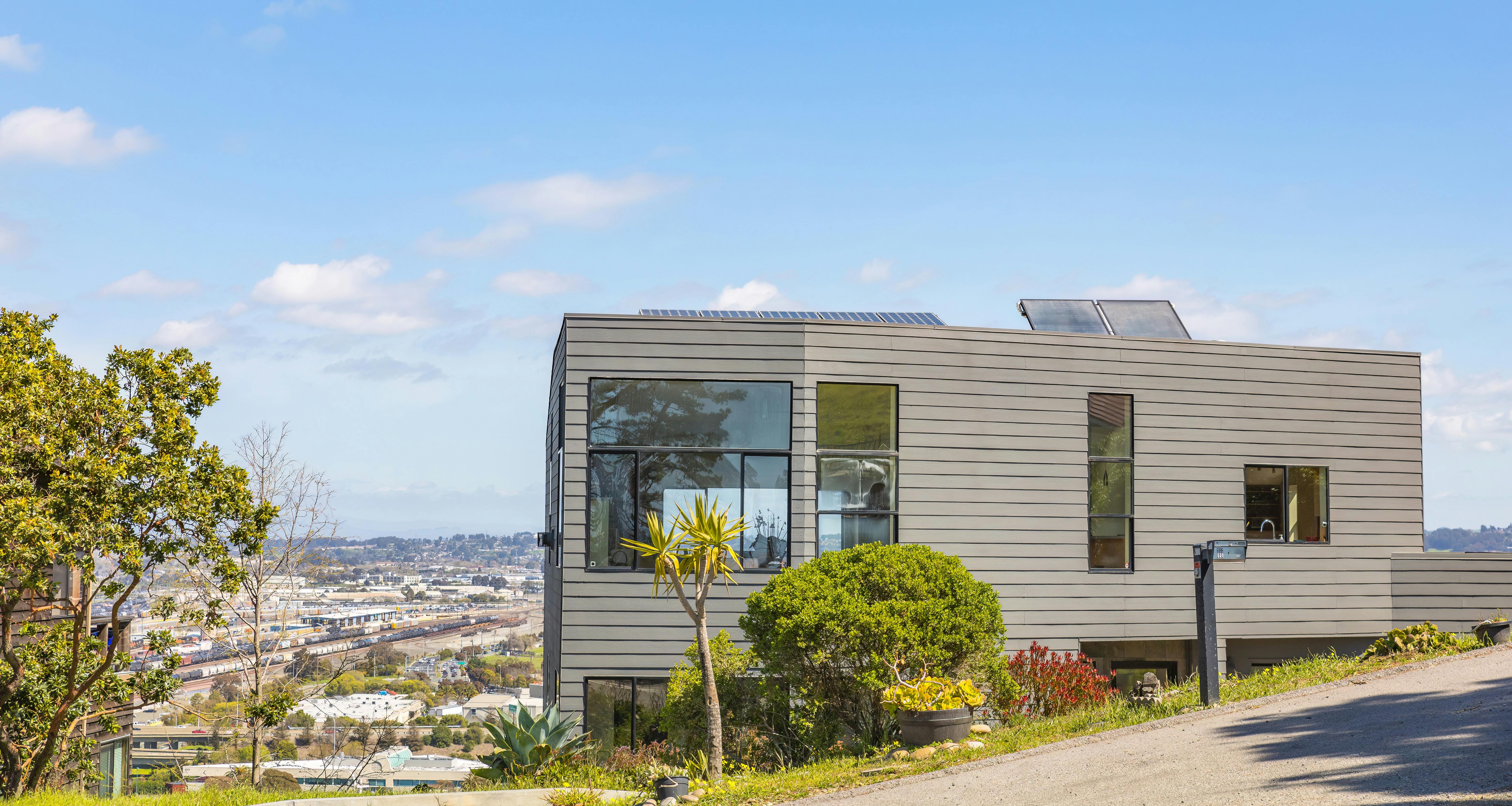 Image depicting a contemporary hillside home with solar panels and city views on a clear summer day.