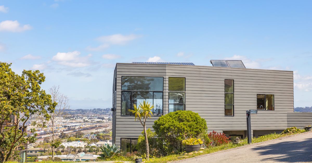 Contemporary hillside home with solar panels and city views on a clear summer day.