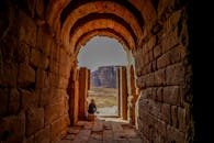 一名妇女坐在历史悠久的石砌拱门下，眼前是广阔的沙漠景观