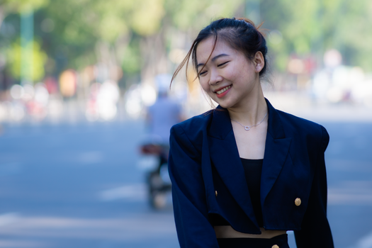 Young woman in navy clothing smiling outdoors on a city street during the day.