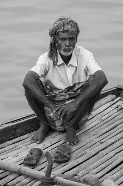 A thoughtful black and white portrait of a man sitting on a bamboo boat.