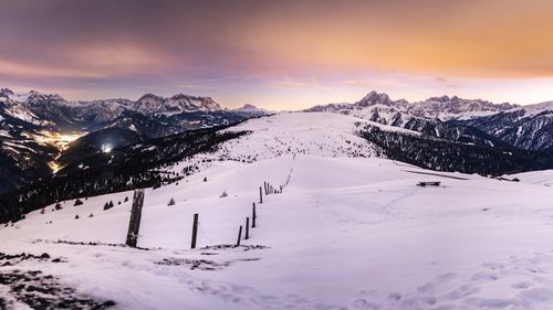 Free Snow-covered mountain landscape with city lights and a vibrant sunset sky in the Dolomites. Stock Photo