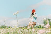 一名妇女坐在田野的凳子上，四周鲜花盛开，她在晴朗的蓝天下享受着户外阳光