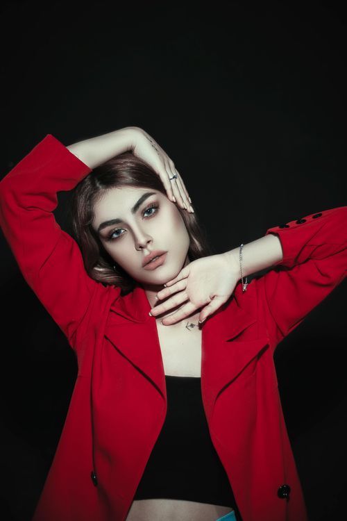 Free Elegant portrait of a woman in a stylish red coat posing indoors with a black background. Stock Photo