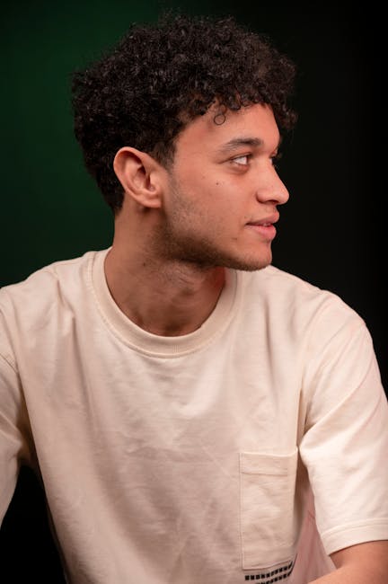 Side profile portrait of a young man with curly hair against a green background.
