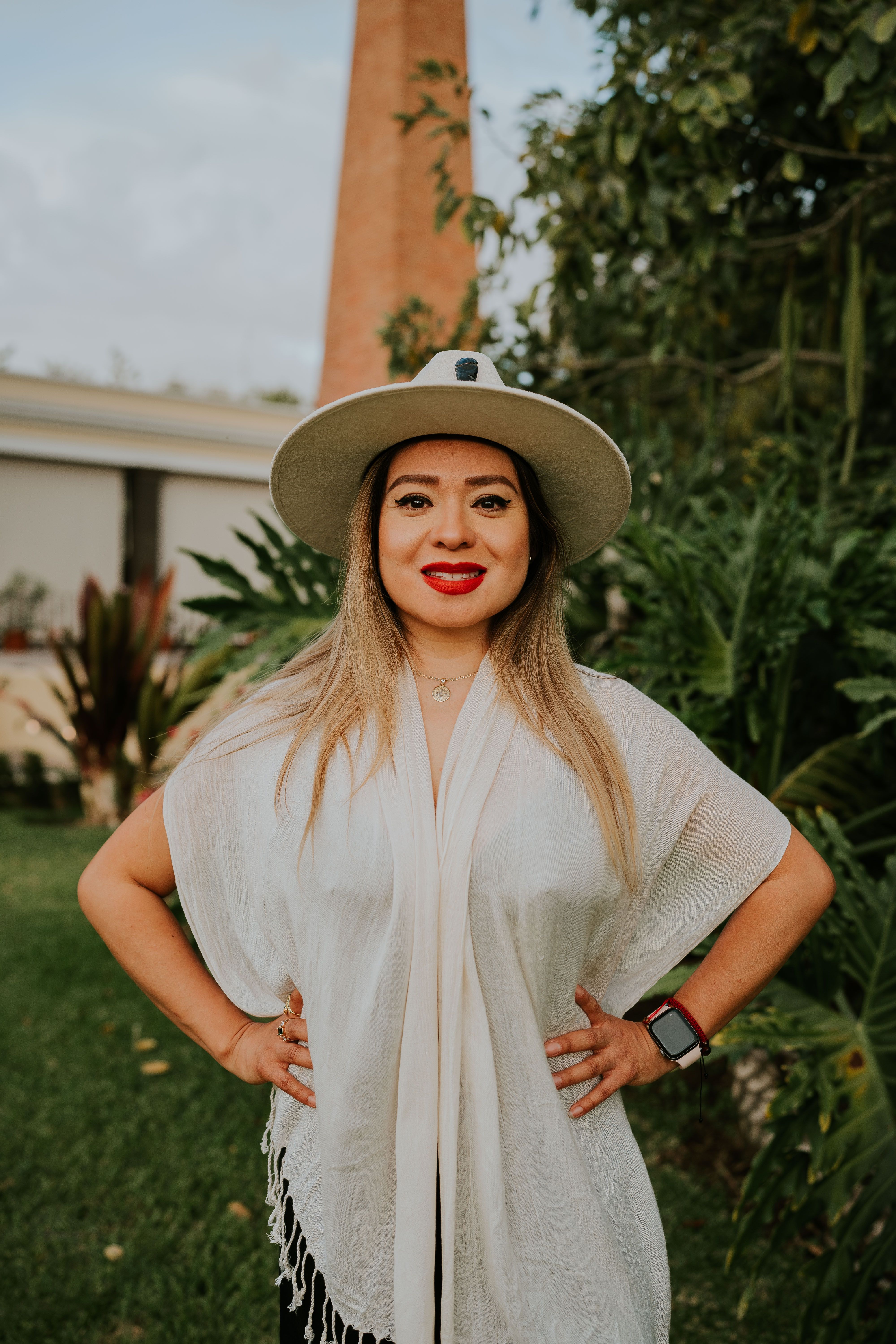 Woman in white clothing and hat posing confidently in an outdoor setting.