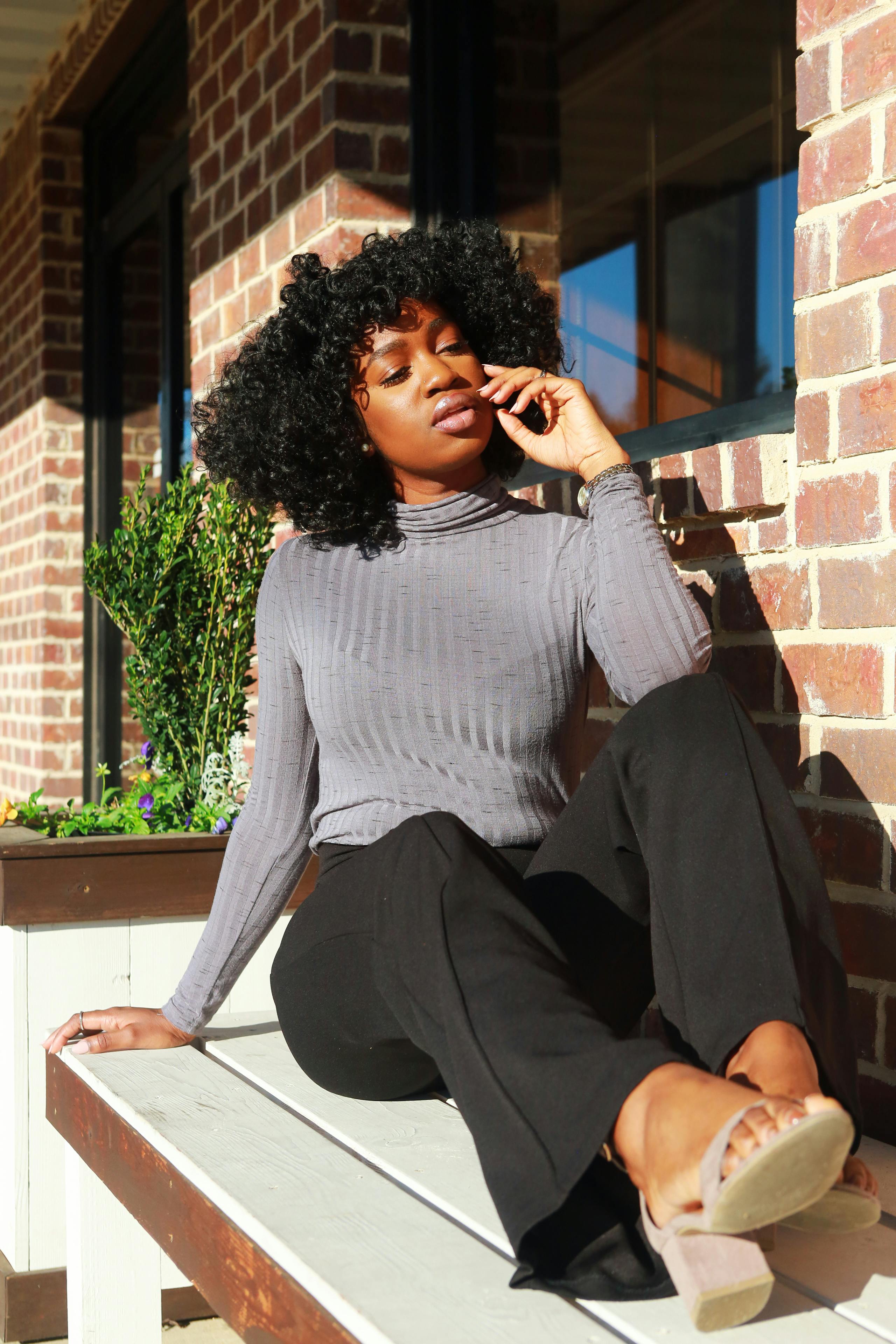 一位时尚女士穿着休闲装，坐在户外的长凳上享受阳光