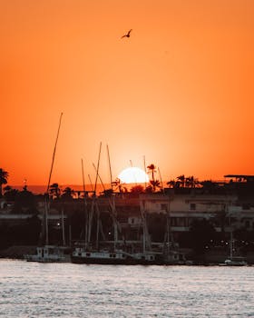 A picturesque sunset in Luxor, Egypt, highlighting the riverfront with sailboats and vibrant skies.