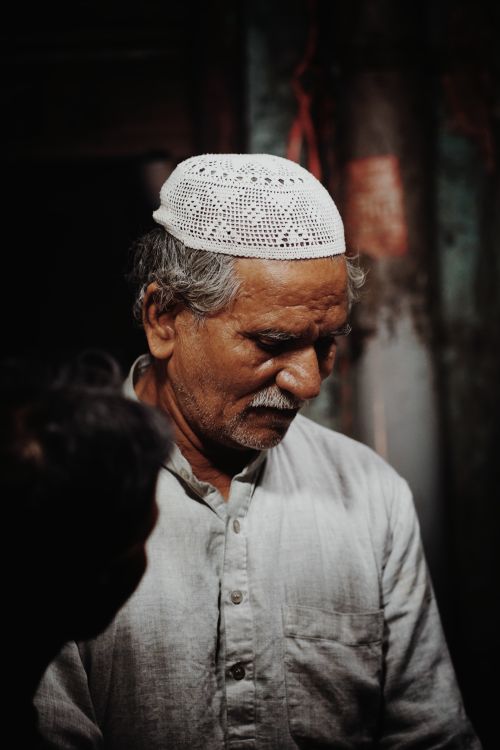 Free Portrait of an elderly man wearing a traditional white cap, deep in thought, captured in a serene moment. Stock Photo
