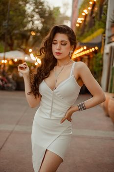 Stylish brunette woman posing in a white dress with urban lights in the background. Perfect for fashion photography.