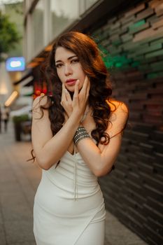 Stylish woman in a white dress posing elegantly in an urban environment during the day.