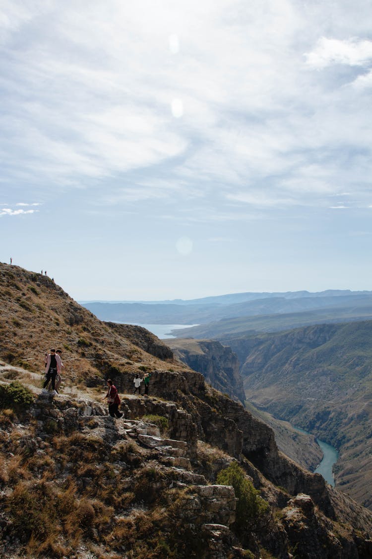 People Hiking On Hills Over River In Valley